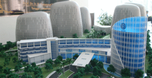 Maket arsitektur gedung kampus modern dengan desain futuristik dan struktur melengkung, dikelilingi elemen lanskap hijau