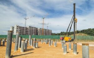 Pekerja konstruksi mengoperasikan alat berat untuk pemasangan tiang pancang di proyek bangunan bertingkat