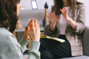 Dua wanita sedang berdiskusi dalam sesi konseling dengan buku catatan terbuka di pangkuan